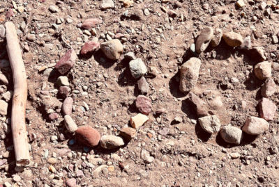 A stick serving as number one and some rocks shaping two zeros for the number 100 on dirt ground.