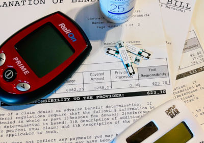 Medical bills with a calculator, blood testing strips, and blood testing meter.