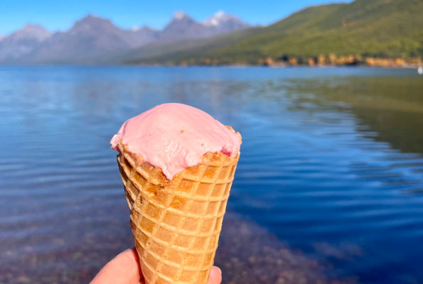 Mostly eaten icecream cone held up in front of Lake McDonald with mountains in the background